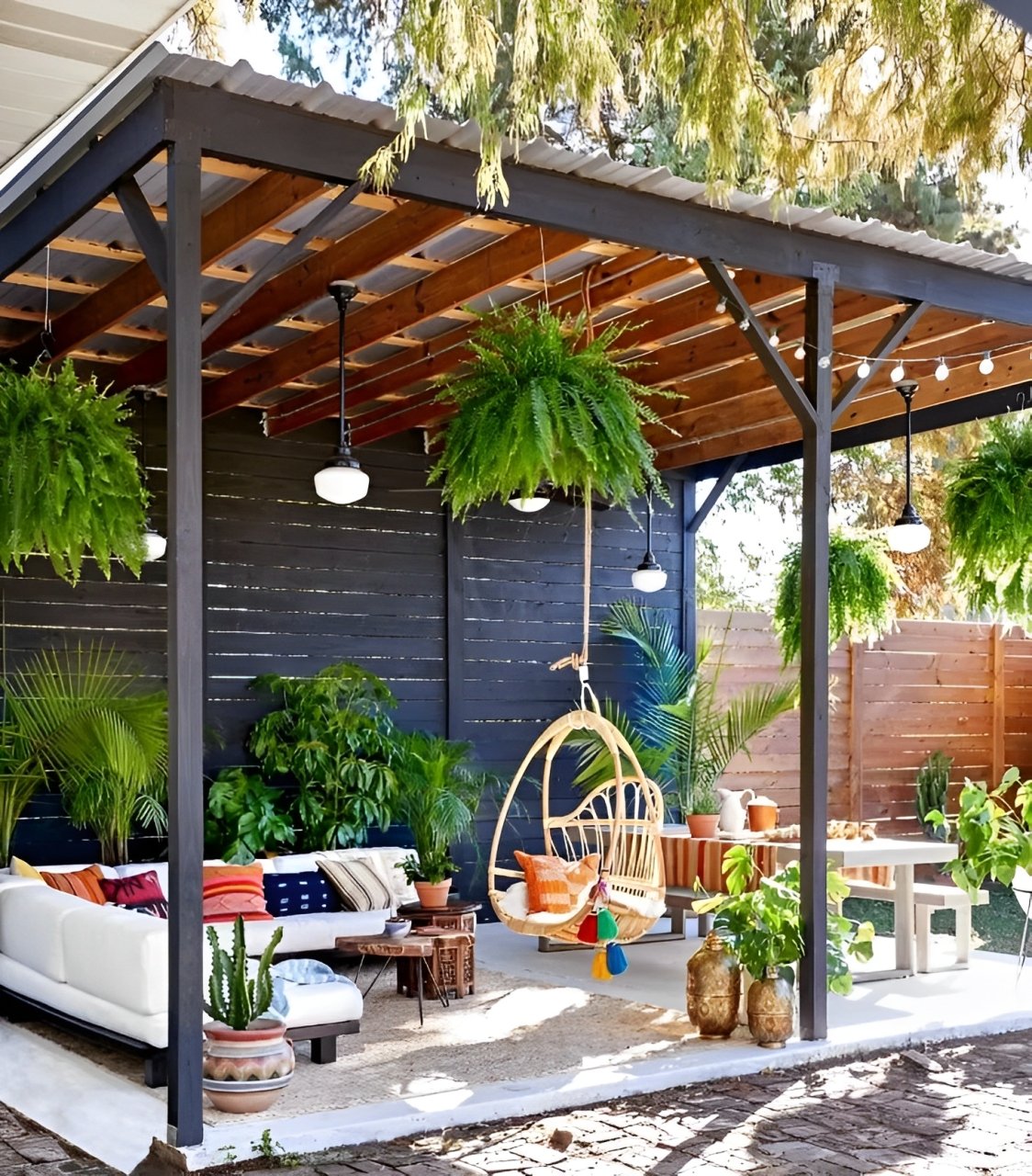 Outdoor patio with a timber pergola, hanging ferns, white lounge seating, and a wicker swing chair.