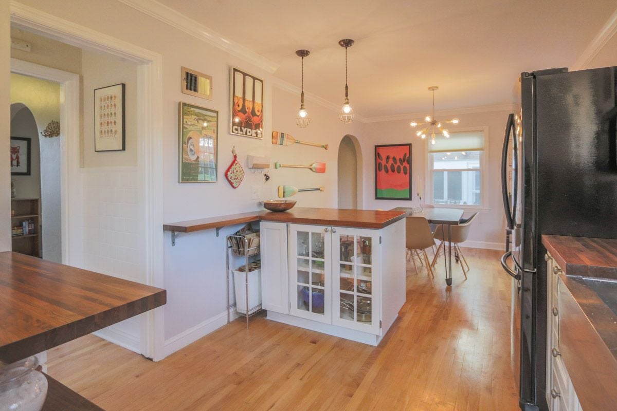 Kitchen with butcher-block counters, a glass-front island, colorful wall art, and a dining nook.