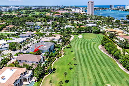 Aerial view of a striped golf course surrounded by homes, with waterfront high-rises in the distance.