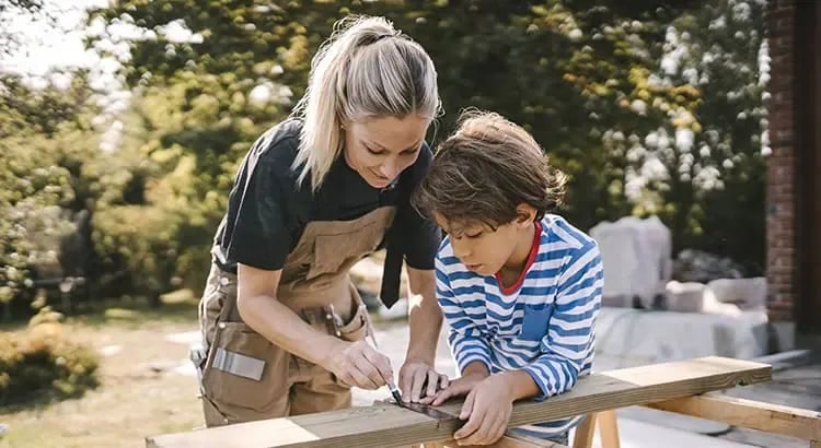 A woman and a young boy working together on a woodworking project. The woman is guiding the boy, indicating a teaching or mentoring moment.