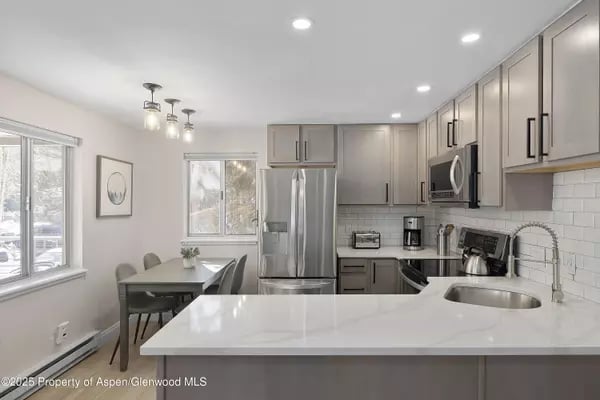 Modern kitchen with gray cabinets, stainless steel appliances, and a large white island beside snowy-view windows.