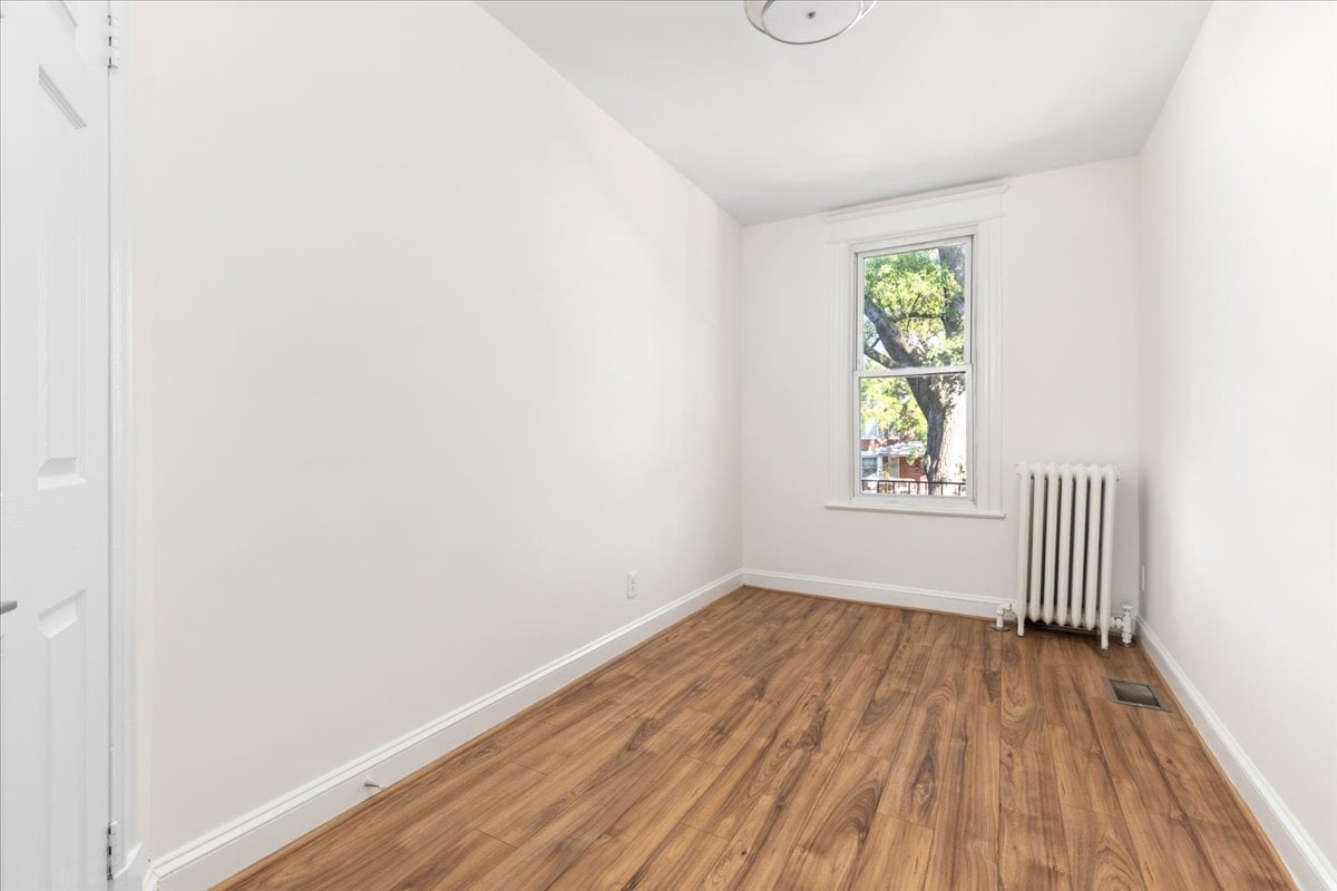 Empty room with wood-look flooring, a window overlooking a tree, and a white radiator.