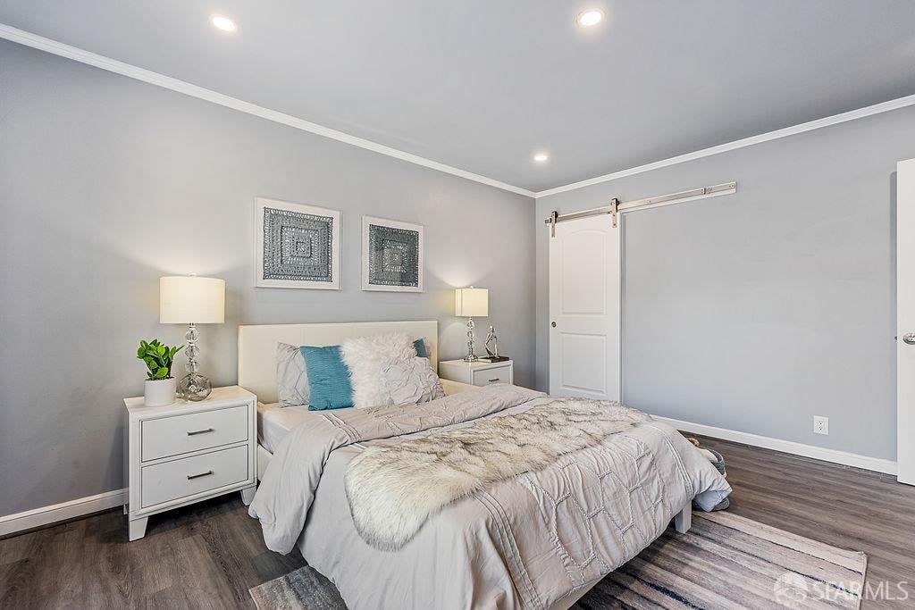 Staged bedroom with pale gray bedding, a teal accent pillow, and a white sliding barn door.