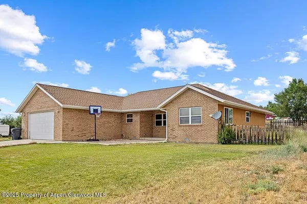 Brick ranch-style house with an attached garage, basketball hoop, and fenced yard.
