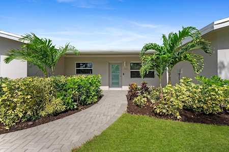 Single-story home entrance framed by palm trees, hedges, and a paved walkway.