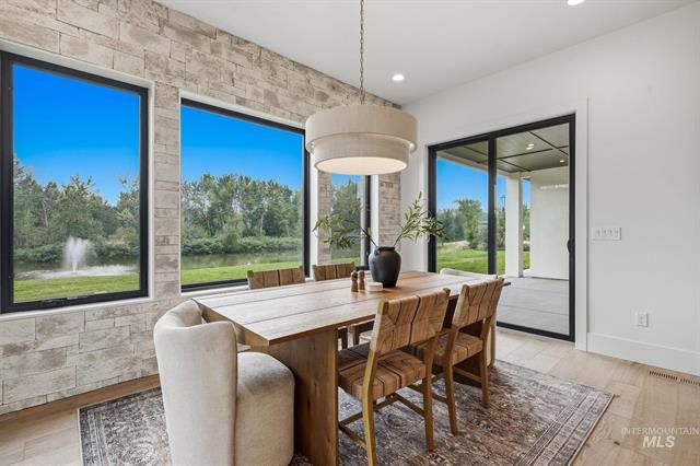 Dining room with a long wood table, stone accent wall, and windows overlooking a pond fountain.