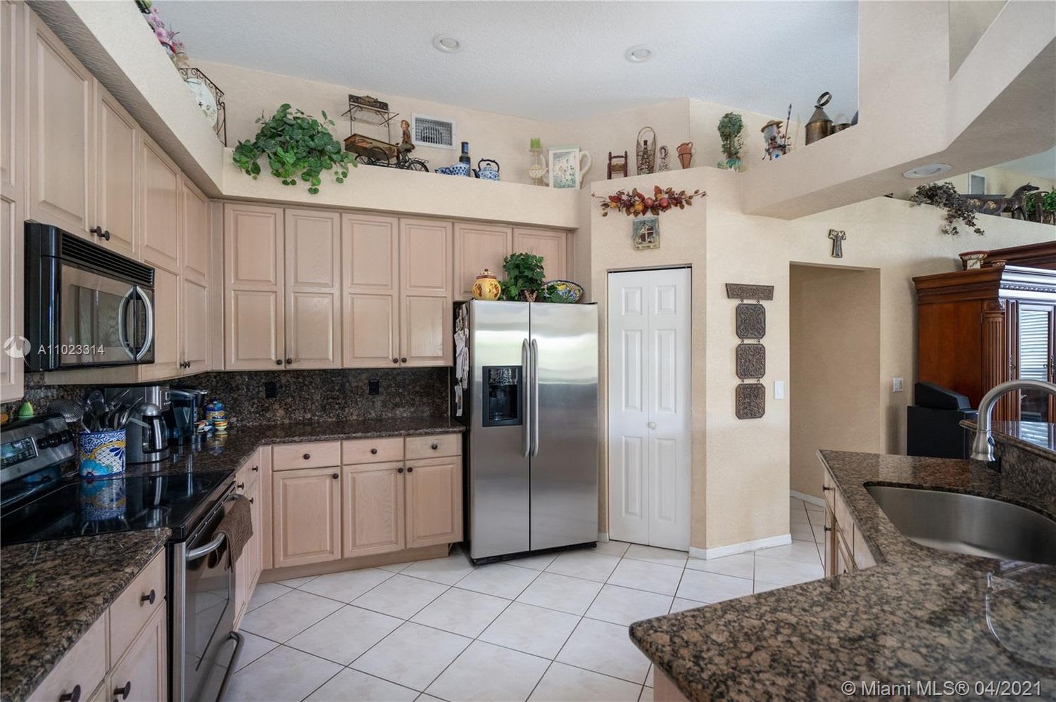 Kitchen with pale wood cabinets, dark granite counters, stainless-steel appliances, and a high display ledge.