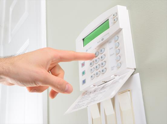 Hand pressing a button on a wall-mounted security alarm keypad with a green display.