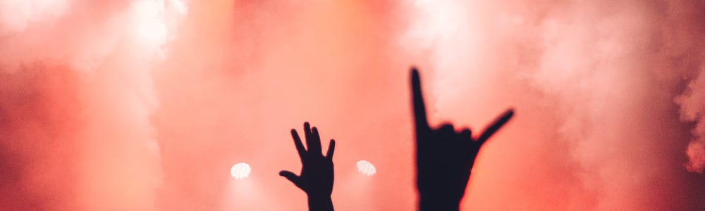 Silhouettes of hands raised at a concert, with a vibrant red and smoky background.