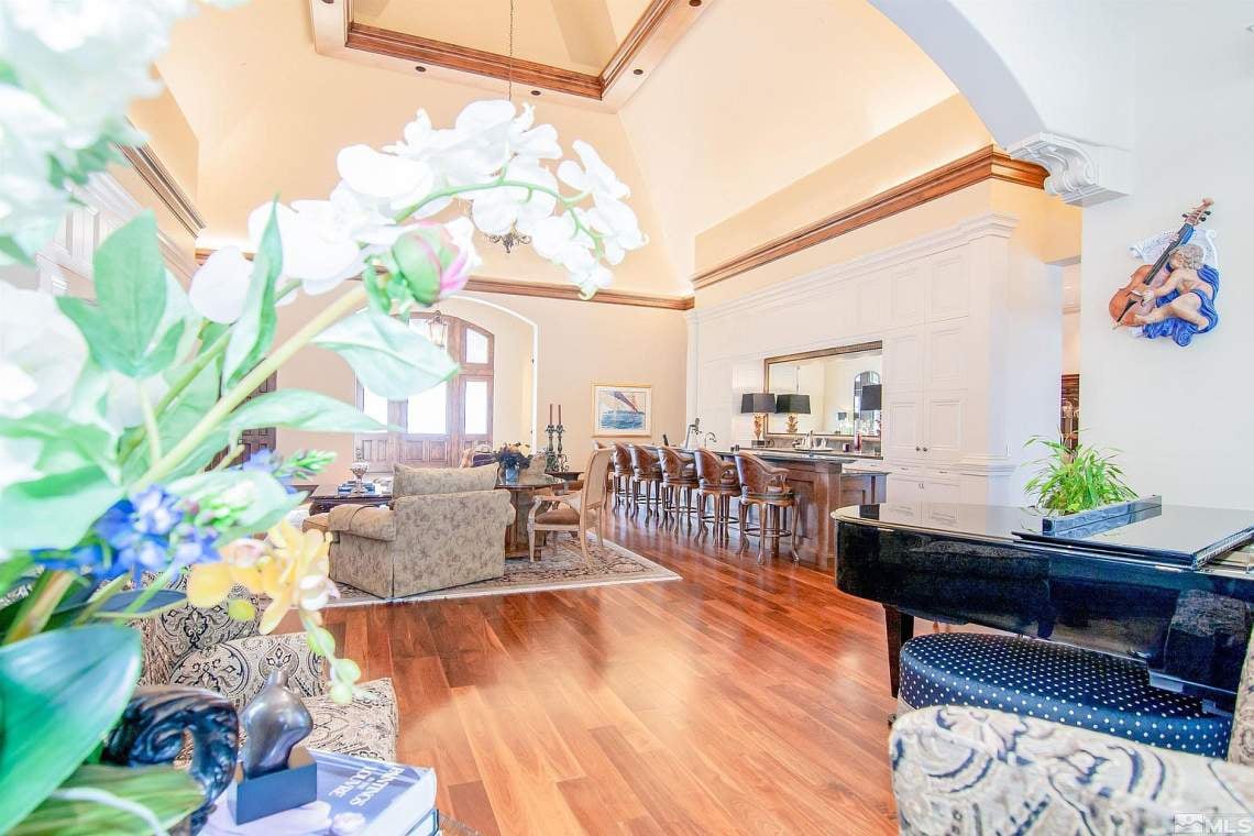 Furnished great room with vaulted ceiling, open kitchen, polished wood floors, and a grand piano.