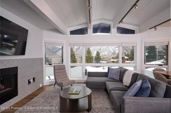 Living room with a gray sectional sofa, fireplace, and wide windows overlooking snowy mountains.