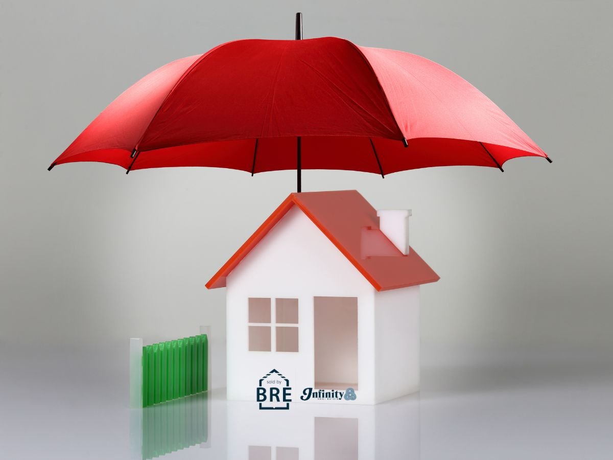 Model house beneath a large red umbrella, beside a short green fence.