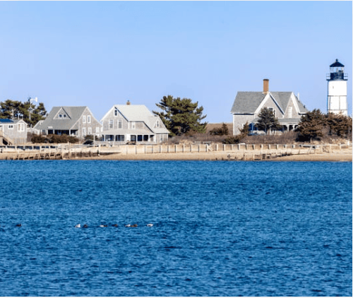 Waterfront homes line the shore, with a white lighthouse at the right.
