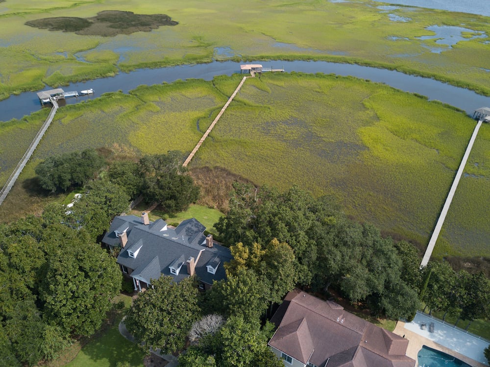 Aerial view of homes beside a tidal river, with long docks extending into surrounding marshland.