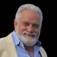 Older man with white hair and a full beard, wearing a blue shirt and cream jacket.