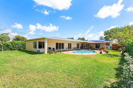 Single-story home with a swimming pool, covered patio, and broad green lawn.