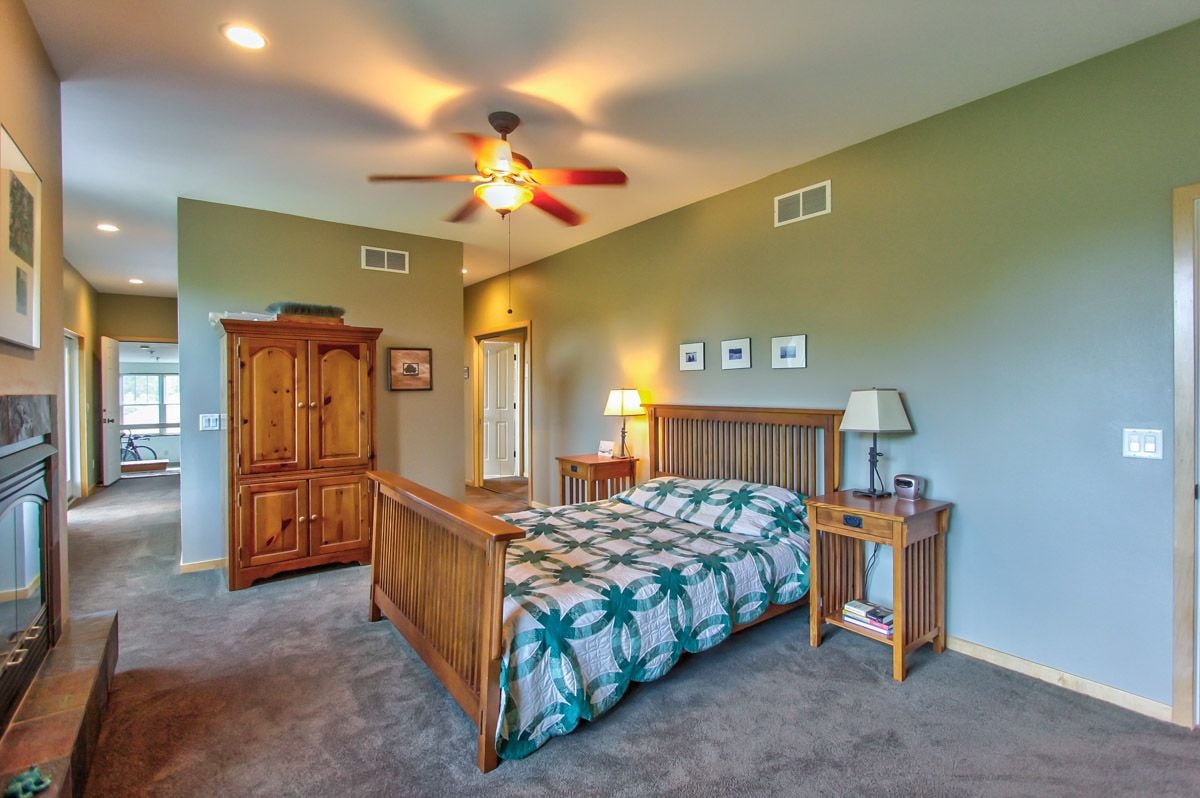 Furnished bedroom with a wooden bed, patterned teal quilt, armoire, and ceiling fan.