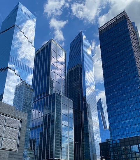 Manhattan skyscrapers rise against a partly cloudy blue sky.