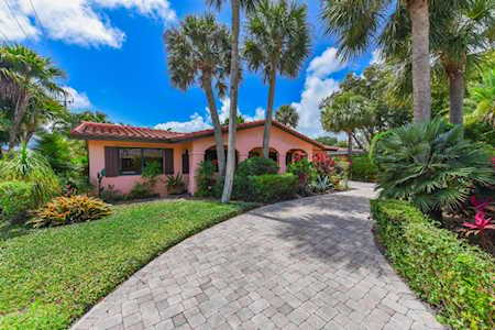 Pink stucco home with a red tile roof, curved paver driveway, and tropical landscaping.