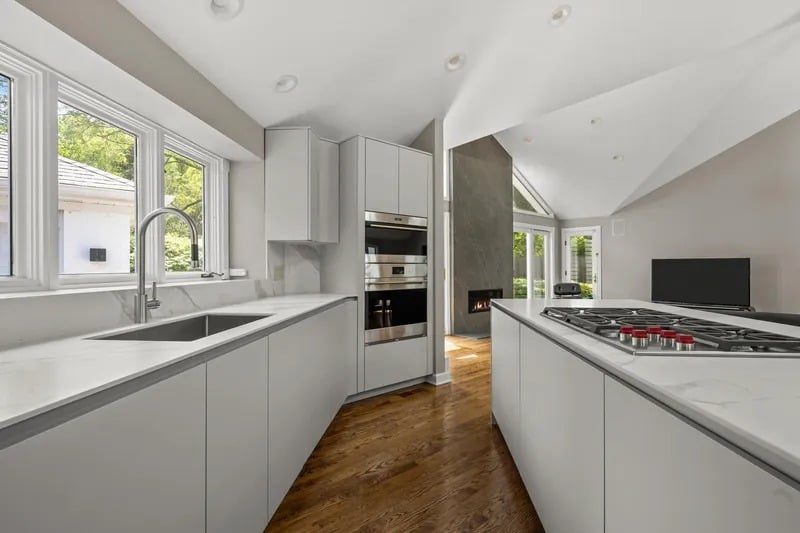 Modern kitchen with a marble island cooktop, double ovens, vaulted ceiling, and warm wood flooring.