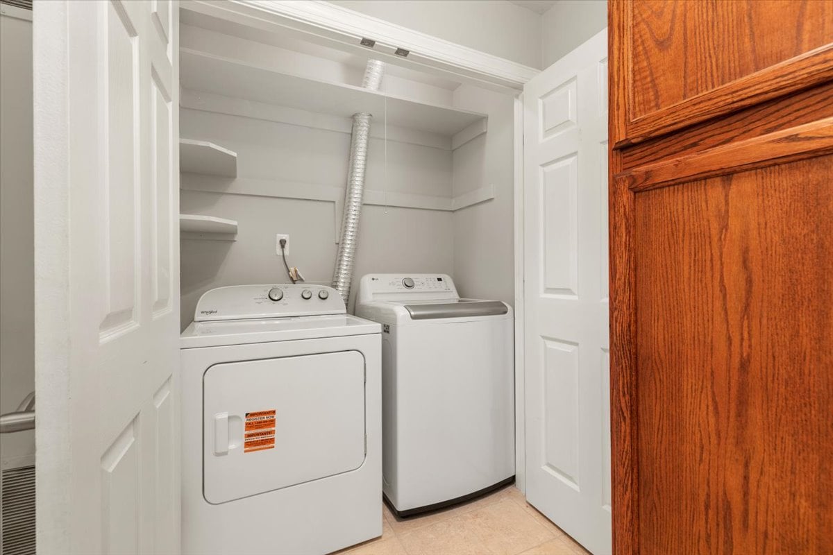 Laundry room with a white dryer and washer beneath built-in shelves.