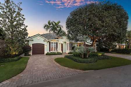 Single-story home with a brick-paved driveway, dark garage door, and mature trees at dusk.