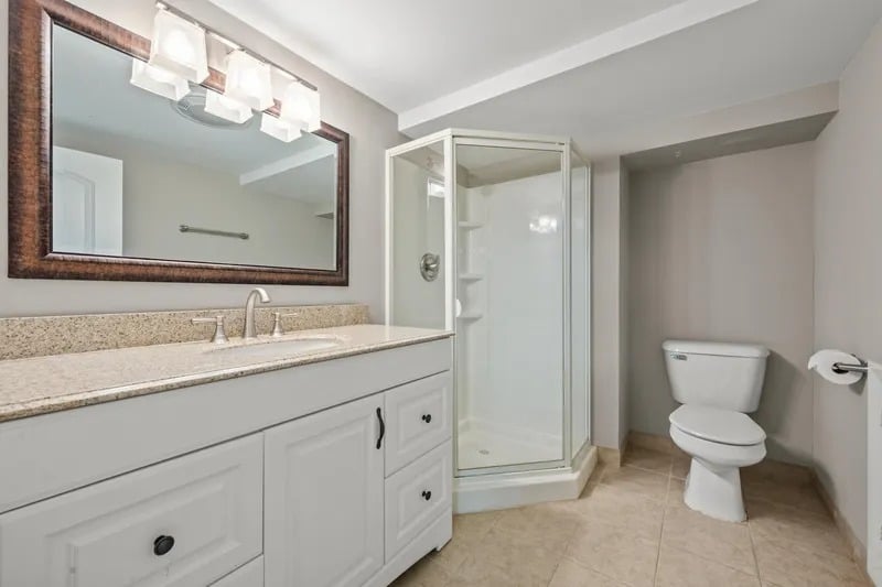 Bathroom with a white vanity, framed mirror, glass shower, and toilet.