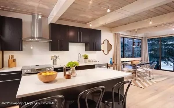 Modern kitchen with a large white island, dark cabinetry, and wood-plank ceiling.
