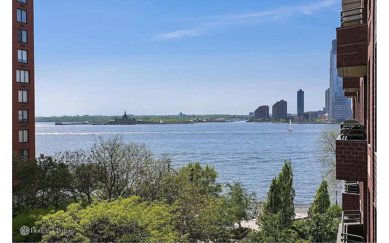 River view framed by brick apartment buildings, with a sailboat and distant skyline.