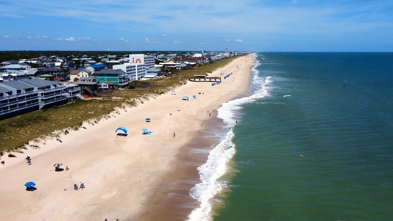 Aerial view of a sandy beach lined with coastal homes beside the ocean.