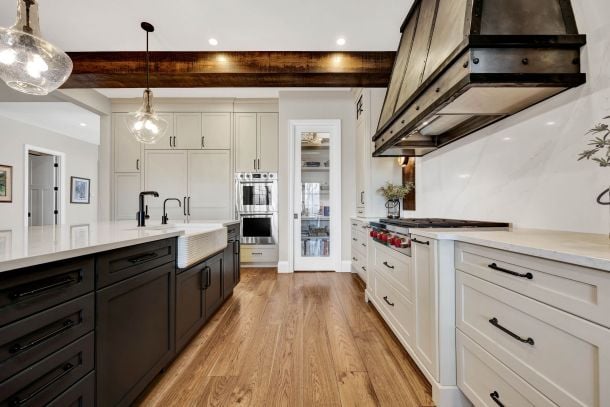 Bright kitchen with a dark island, white cabinets, wood floors, and a prominent timber range hood.