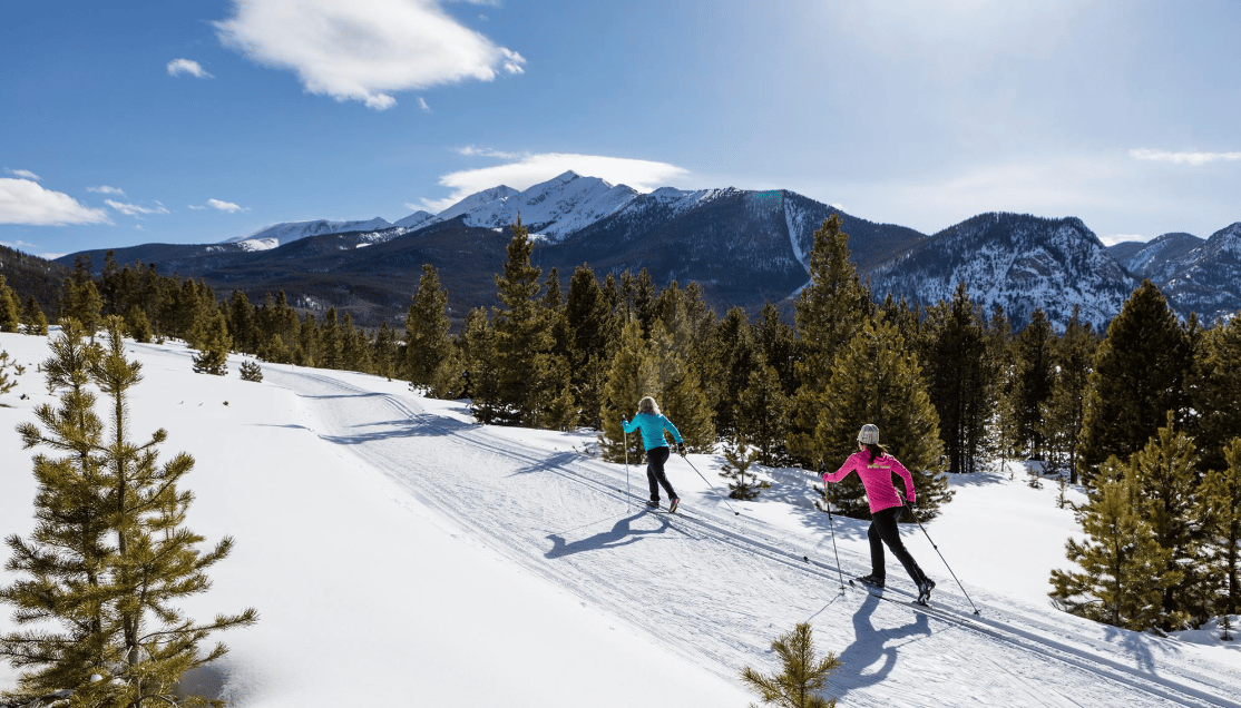 a pair of nordic skiers making their way across a snowy trail on a clear mountain day.