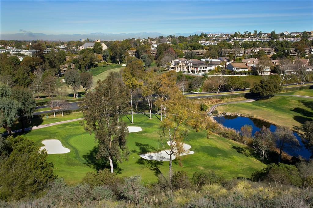 Aerial view of a golf course with ponds, sand bunkers, and homes beyond.
