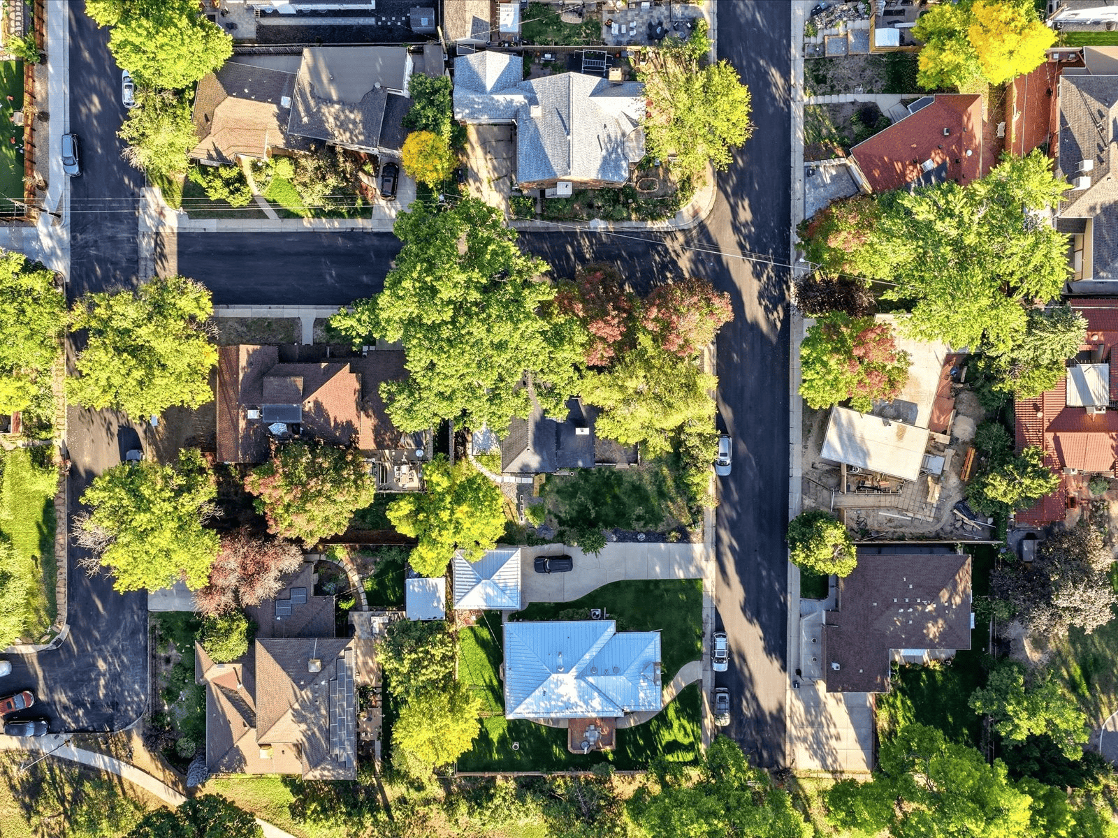 Aerial view of a blue-roofed home on a leafy residential block with intersecting streets.