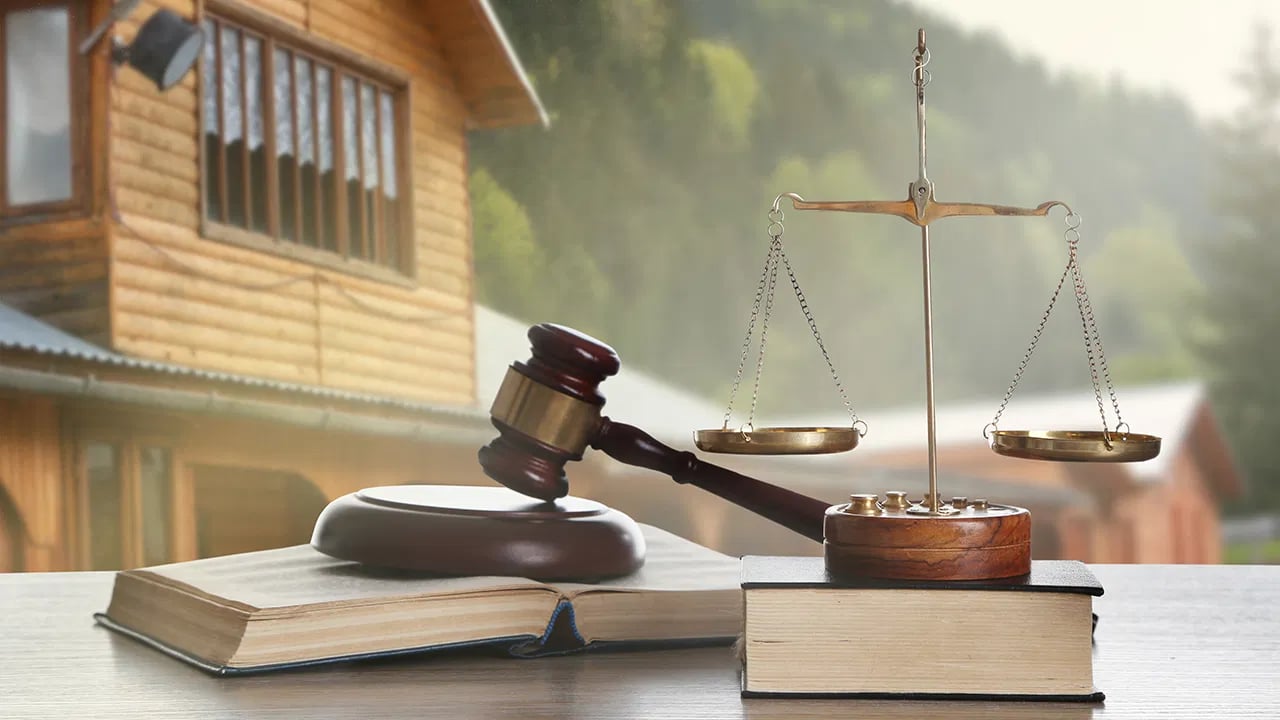 Gavel and balanced scales on law books, with a wooden house in the background.