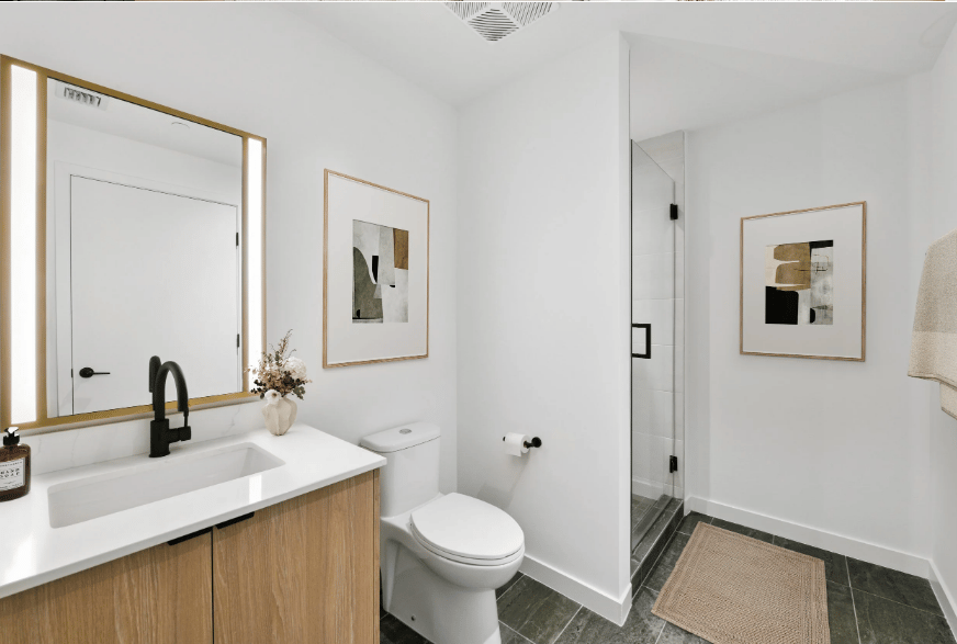 Modern bathroom with a gold-framed mirror, wood vanity, and glass-enclosed shower.