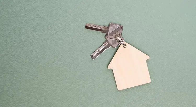 A keychain with house-shaped tags on a green background, symbolizing home ownership or real estate sales.