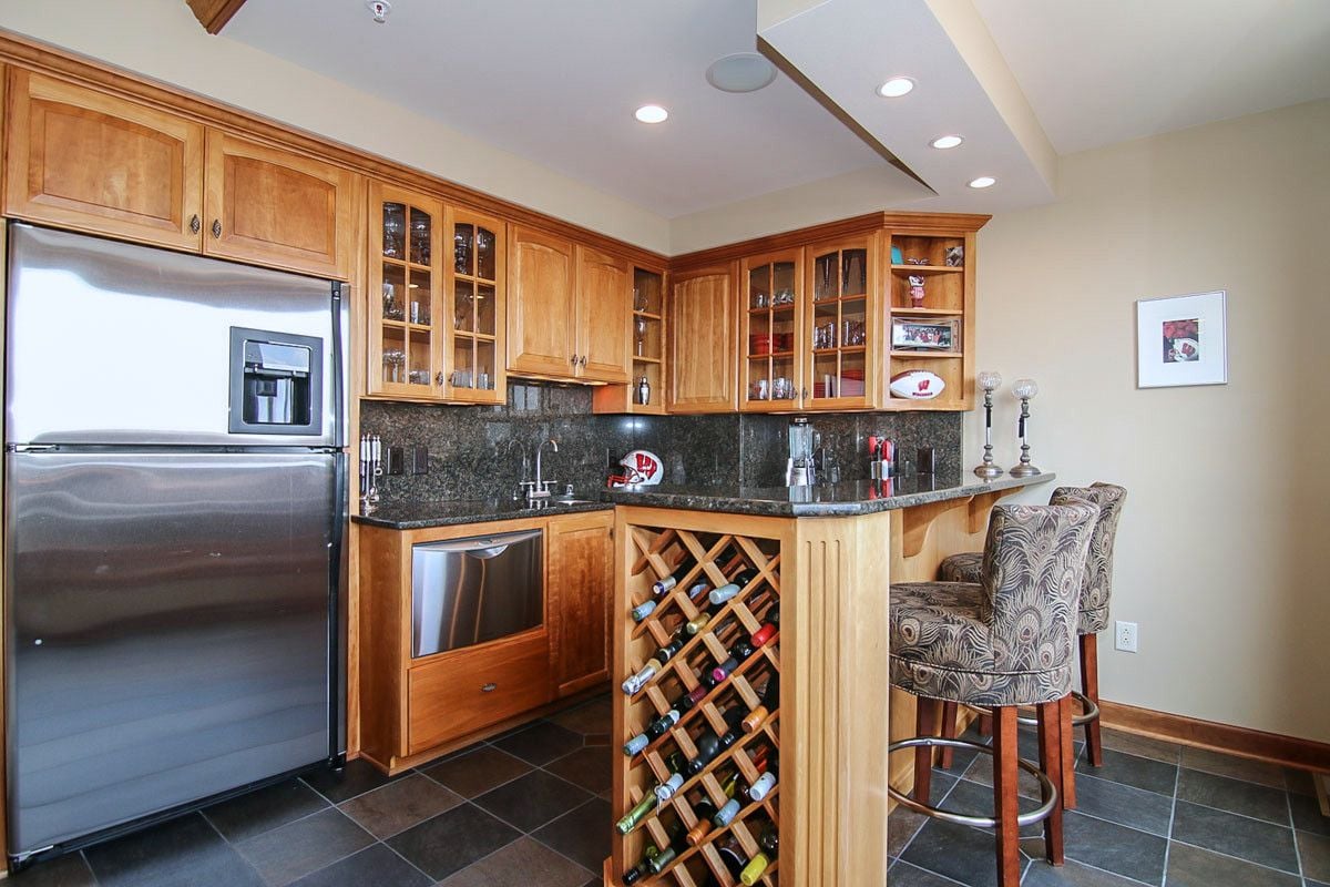 Penthouse kitchen with warm wood cabinets, dark stone counters, a built-in wine rack, and upholstered bar stools.