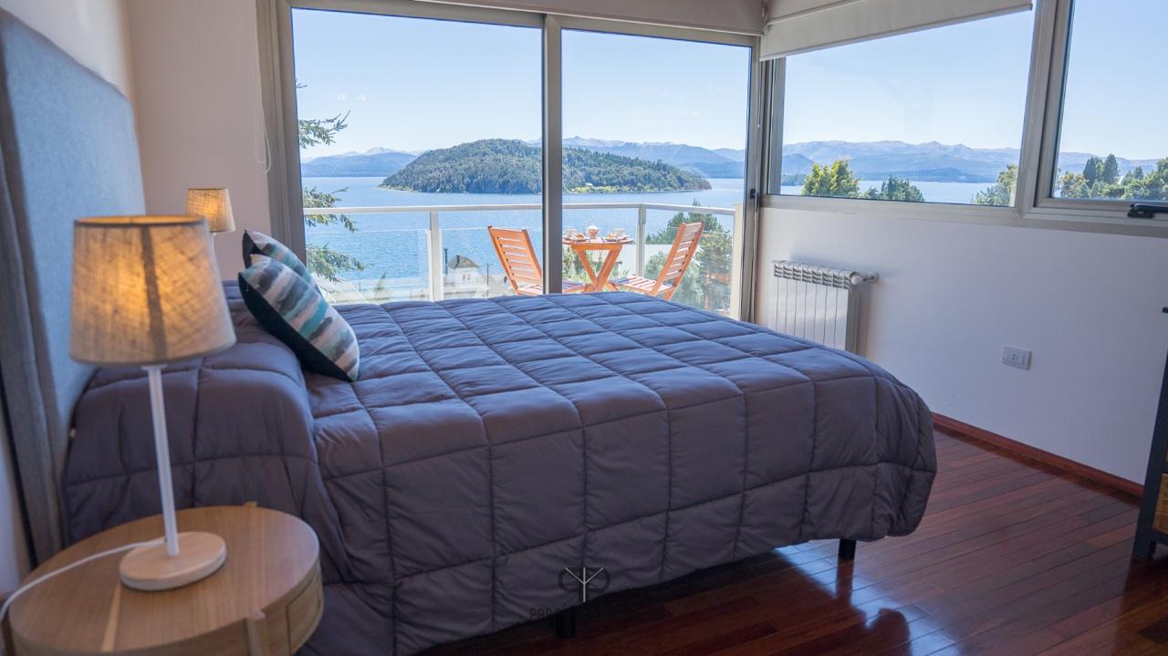Furnished bedroom with a lake and mountain view through sliding glass doors.