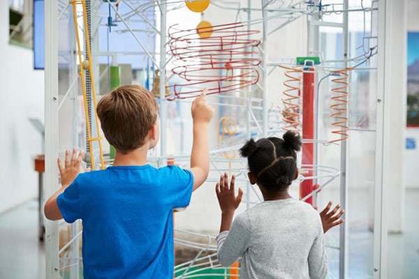 Two children explore a colorful ball-track exhibit at an indoor science museum.