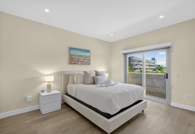 Furnished bedroom with a white bed, lit bedside lamp, and sliding glass door to a balcony.