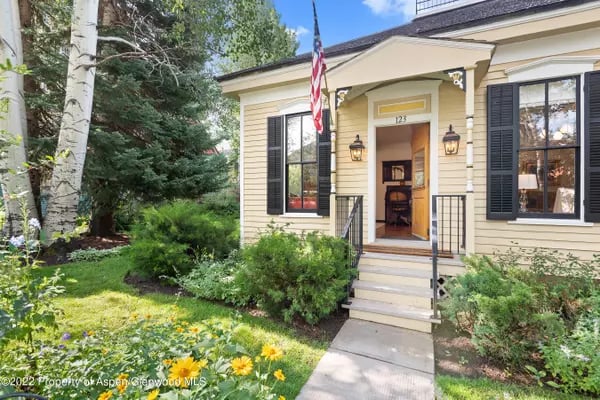 Yellow house with a covered entry, black shutters, and a landscaped garden.