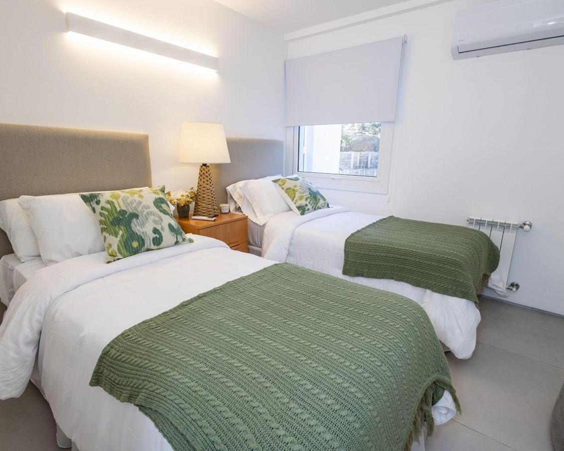 Bedroom with two single beds, green throws, patterned cushions, and a shared bedside table.