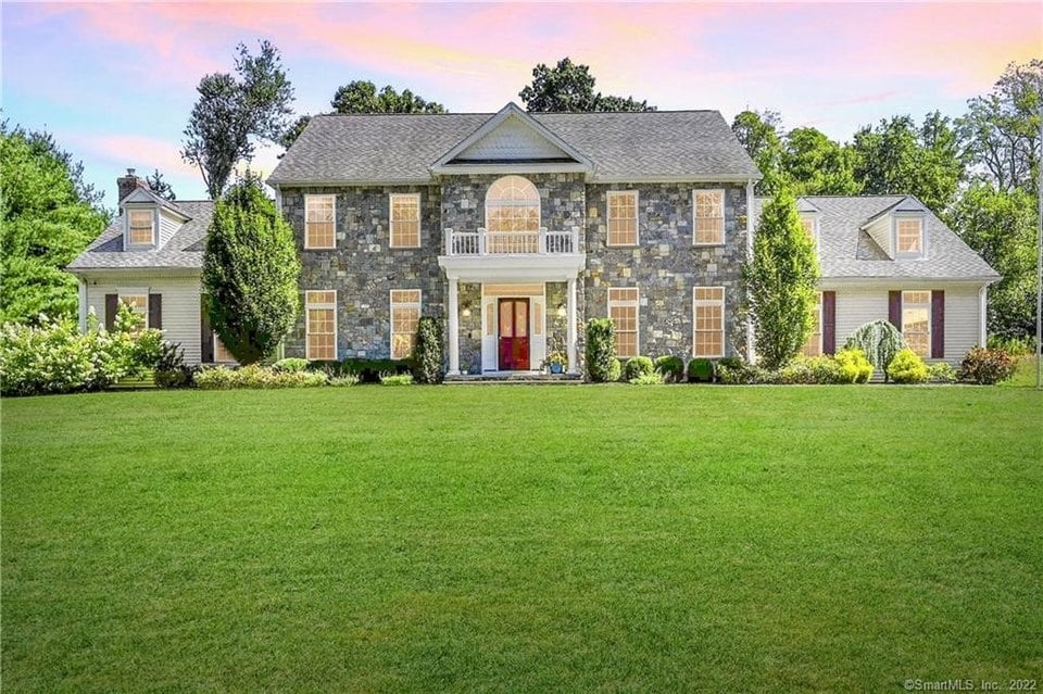 Large stone-and-siding home with a symmetrical facade, red front door, and broad green lawn.