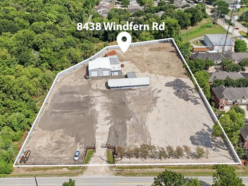 Aerial view of a cleared parcel outlined in white, with small structures and trees along its edges.