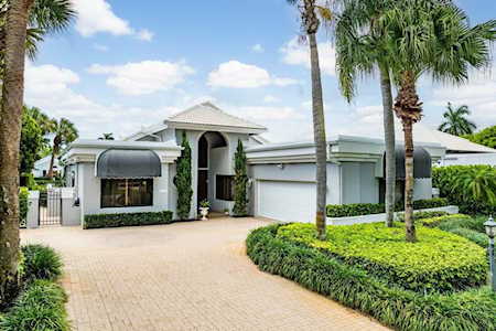 Single-story stucco home with an arched entry, two-car garage, paver driveway, and palm-lined landscaping.