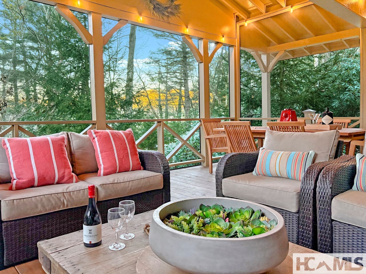 Screened porch with wicker seating and outdoor dining overlooking the trees at 464 Franklin Road, Highlands NC