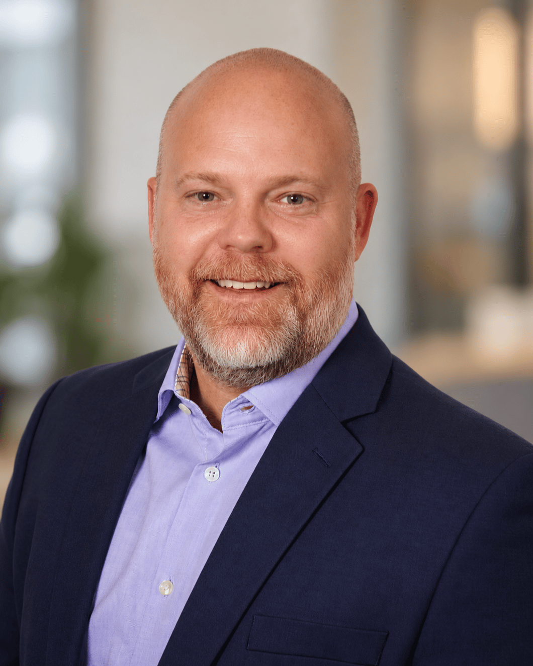 Jeremy Oakford smiling in a navy suit and lavender shirt.