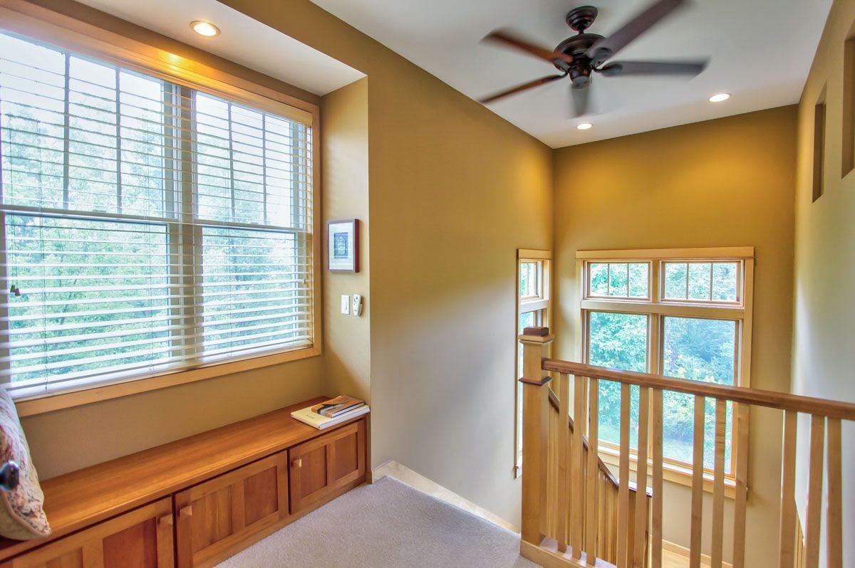 Upper-floor landing with a built-in window bench, tall windows, and a wooden stair railing.