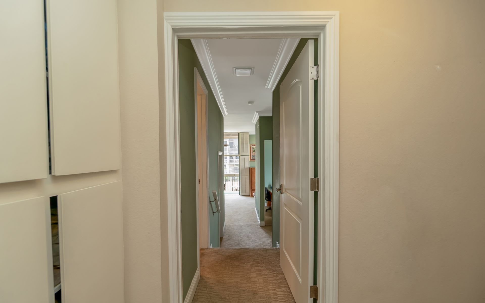 Interior hallway with green walls, white crown molding, carpet, and open doors.
